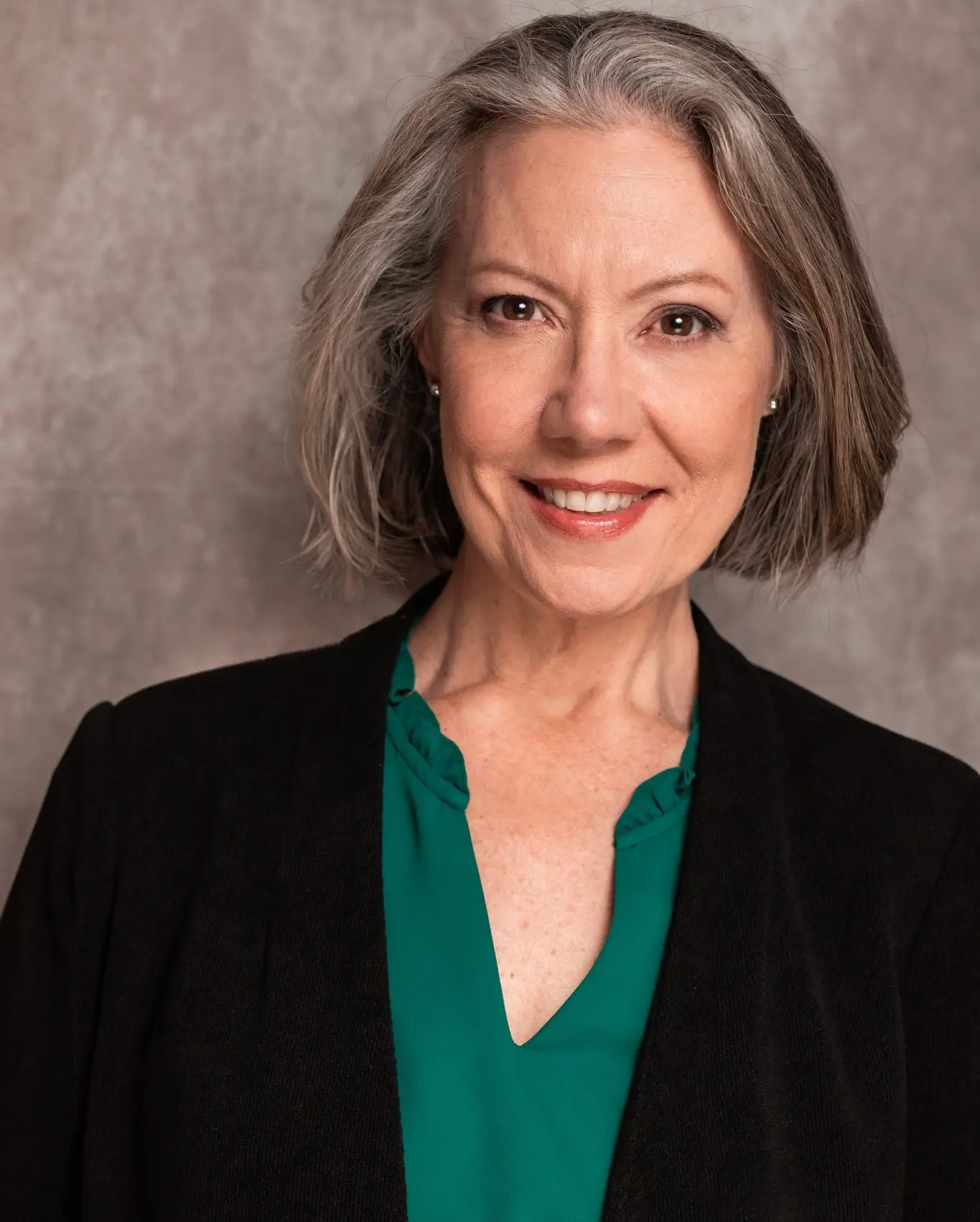 Headshot with green shirt, black jacket, and gray background